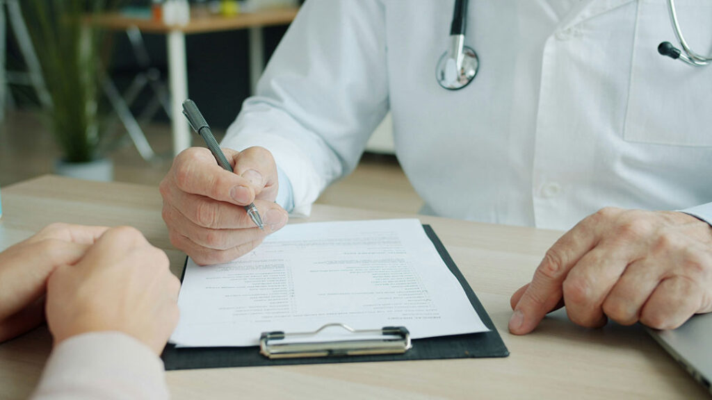 Arzt trägt handschriftlich Befunde in die Patientenakte einer Patientin ein